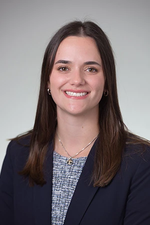 Dr. Roussel in navy blazer smiling in professional headshot on light gray background.